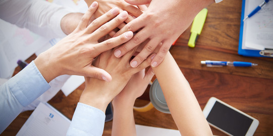 Mehrere Hände, die über einem Tisch mit Seminarmaterialien aufeinangergelegt werden