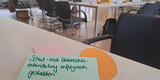 auf einem Tisch liegende Moderationkarten mit der Aufschrift "Schul- und Unterrichtsentwicklung". Im Hintergrund stehen mehrere Seminartische